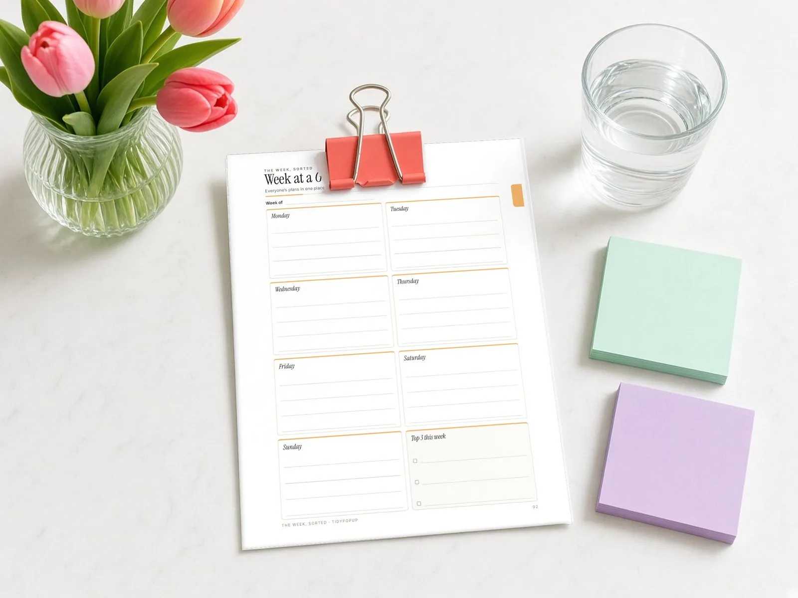 Illustrative styled scene: printed Week at a Glance page held with a binder clip on a kitchen counter